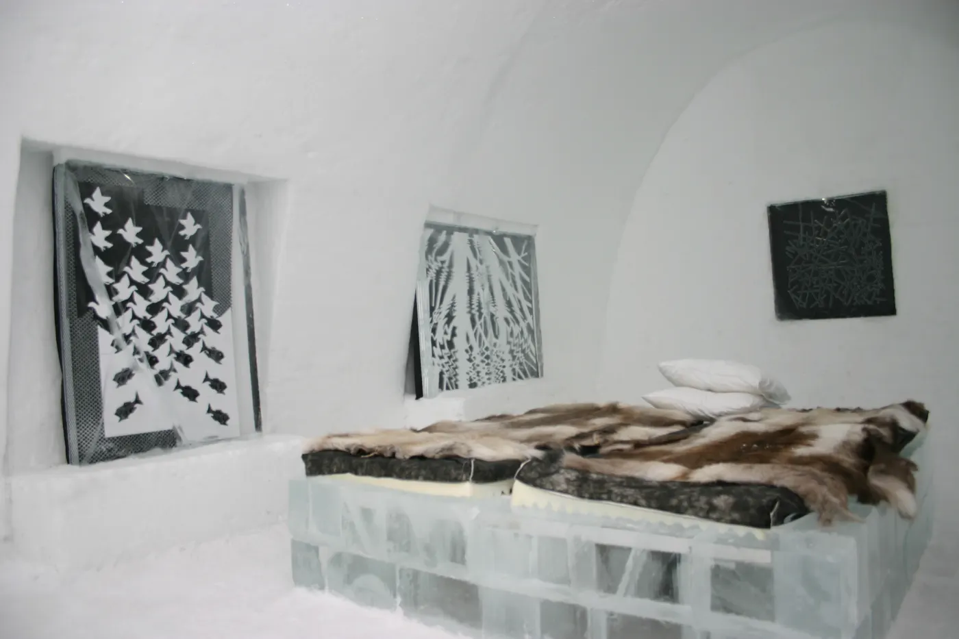 Pokój w Icehotelu – łóżko z bloków lodu przykryte skórami reniferów i lodowe ściany z płaskorzeźbami