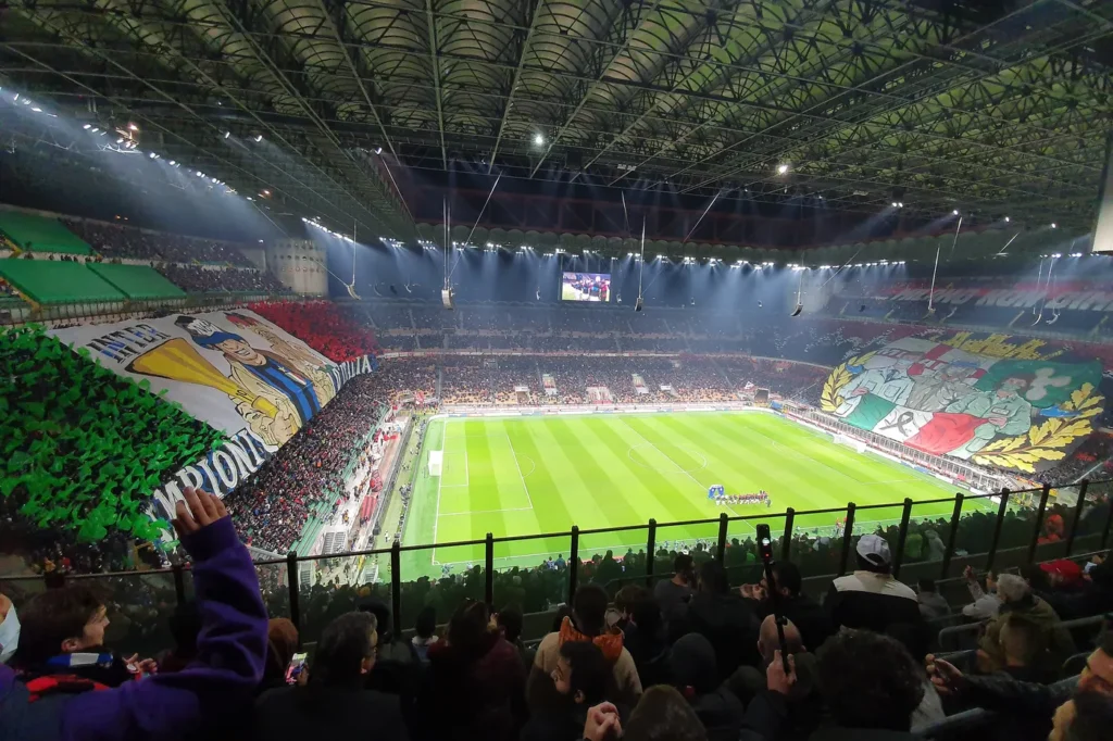 Wypełniony stadion San Siro w Mediolanie podczas derbów Milanu z Interem, z oprawami kibiców na obu trybunach za bramkami