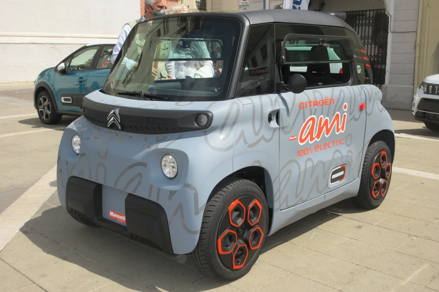 Citroën Ami w jasnoniebieskim kolorze z czerwonymi felgami stoi na placu w mieście