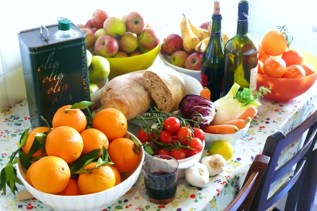 Stół z produktami diety śródziemnomorskiej – oliwą, warzywami, owocami cytrusowymi, chlebem i czosnkiem