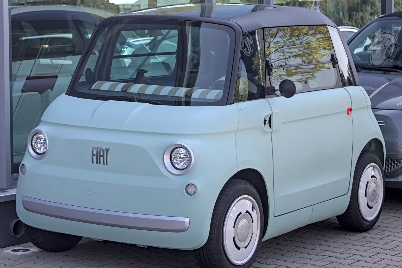 Miętowy Fiat Topolino z ciemnym dachem zaparkowany przed salonem samochodowym