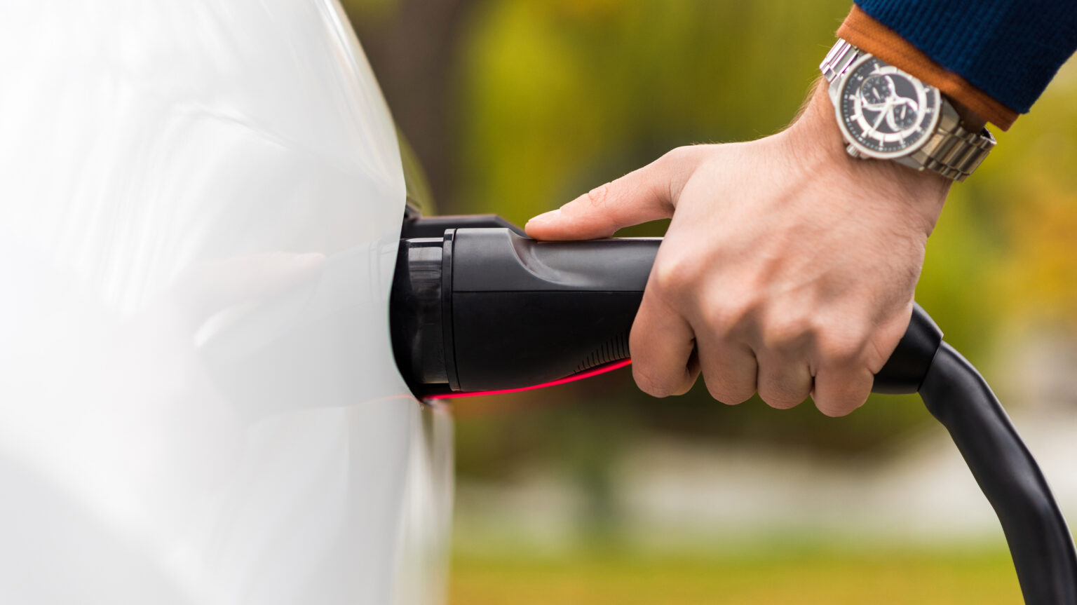 Mężczyzna podłącza wtyczkę ładowarki do gniazda samochodu elektrycznego