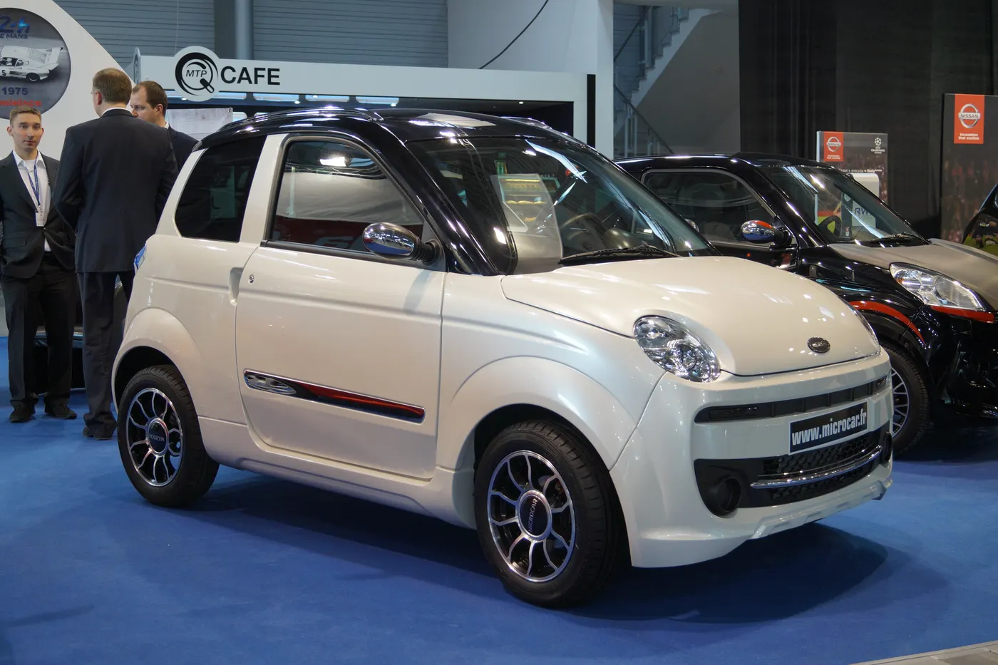 Biały Microcar M.Go z czarnym dachem na stoisku targów motoryzacyjnych