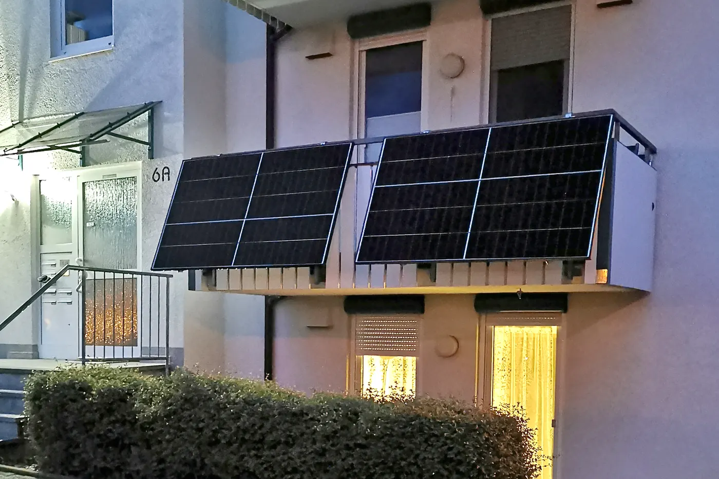Dwa panele fotowoltaiczne odchylone od balustrady balkonu na parterze budynku