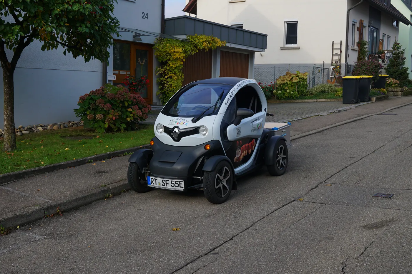 Renault Twizy zaparkowany przy krawężniku na ulicy osiedla domów jednorodzinnych