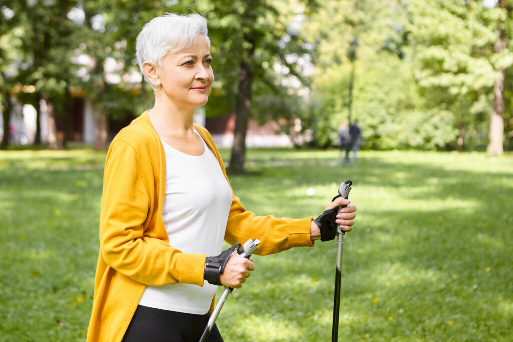Zdrowy styl życia – zasady i zdrowe nawyki, które poprawiają samopoczucie Zdrowy styl życia – starsza kobieta maszeruje z kijkami do nordic walking w parku
